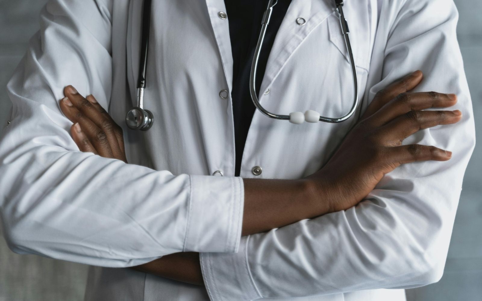 Médico de jaleco branco com os braços cruzados e estetoscópio no pescoço